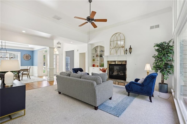 living room with light hardwood / wood-style flooring, crown molding, decorative columns, a fireplace, and ceiling fan