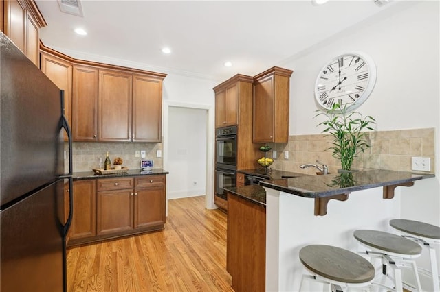 kitchen with black appliances, a kitchen bar, light hardwood / wood-style floors, and tasteful backsplash