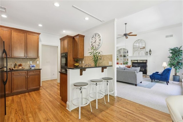 kitchen with kitchen peninsula, decorative backsplash, ceiling fan, a kitchen bar, and light wood-type flooring