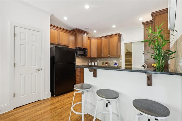 kitchen with decorative backsplash, a breakfast bar area, kitchen peninsula, black appliances, and light hardwood / wood-style floors