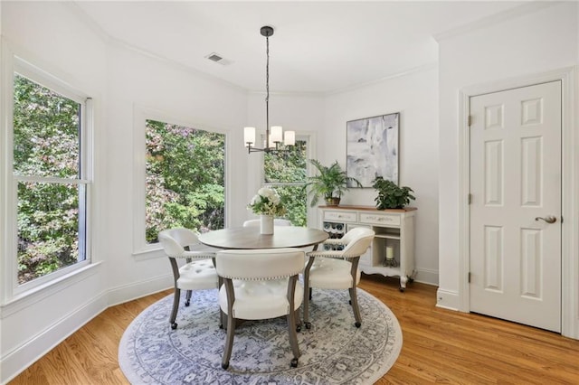 dining area featuring light hardwood / wood-style flooring, ornamental molding, a notable chandelier, and plenty of natural light