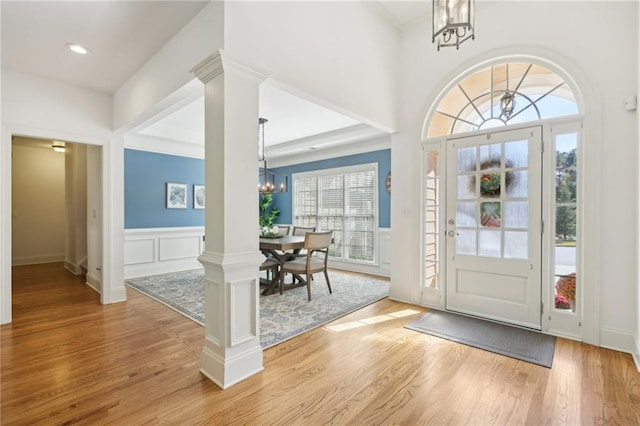 foyer featuring a notable chandelier, ornate columns, light hardwood / wood-style floors, and plenty of natural light