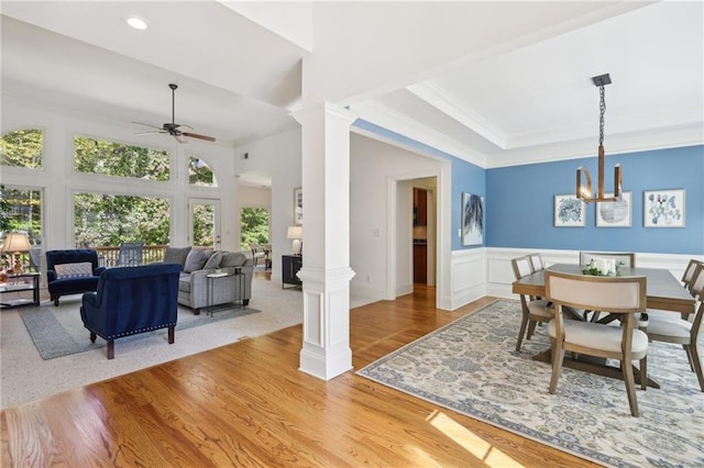 dining space featuring light hardwood / wood-style flooring, ornamental molding, ceiling fan with notable chandelier, and decorative columns