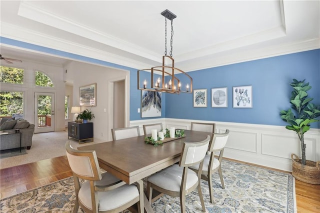 dining space with light hardwood / wood-style floors, crown molding, a tray ceiling, and ceiling fan with notable chandelier