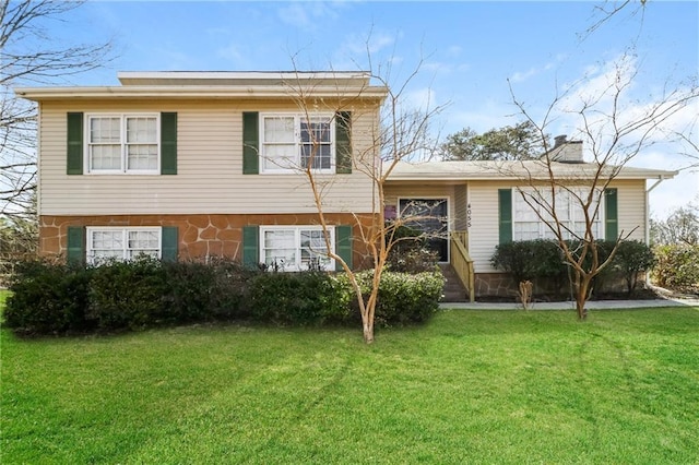 split level home with a front lawn, stone siding, and a chimney