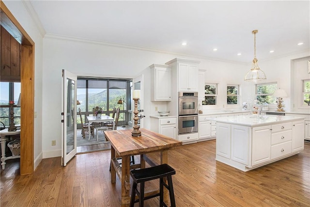kitchen featuring stainless steel double oven, light countertops, ornamental molding, light wood-type flooring, and white cabinetry