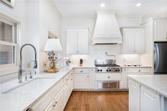 kitchen featuring stainless steel appliances, a warming drawer, a sink, premium range hood, and white cabinets