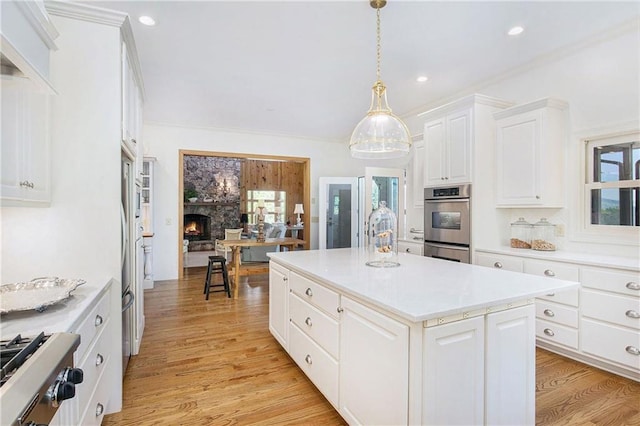 kitchen with appliances with stainless steel finishes, a fireplace, a kitchen island, light wood-style flooring, and white cabinets