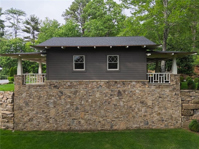 view of side of home featuring stone siding, a yard, and roof with shingles