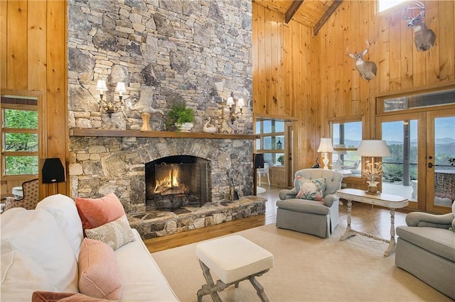 living room with high vaulted ceiling, healthy amount of natural light, wood walls, a stone fireplace, and wood ceiling with exposed beams