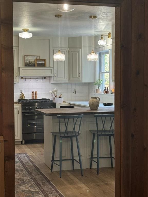 kitchen with a kitchen bar, hardwood / wood-style floors, backsplash, and range with gas cooktop