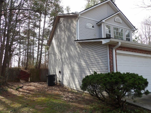 view of side of home featuring an attached garage, fence, brick siding, and central AC