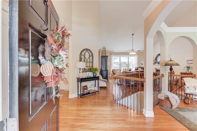 foyer featuring ceiling fan, arched walkways, baseboards, ornamental molding, and light wood finished floors