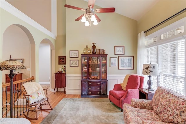 living area featuring arched walkways, a wainscoted wall, ceiling fan, vaulted ceiling, and light wood-style floors