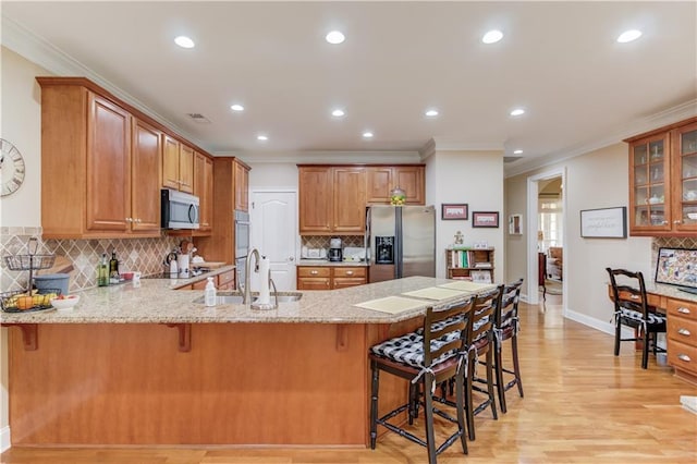 kitchen with appliances with stainless steel finishes, glass insert cabinets, a sink, a peninsula, and a kitchen bar