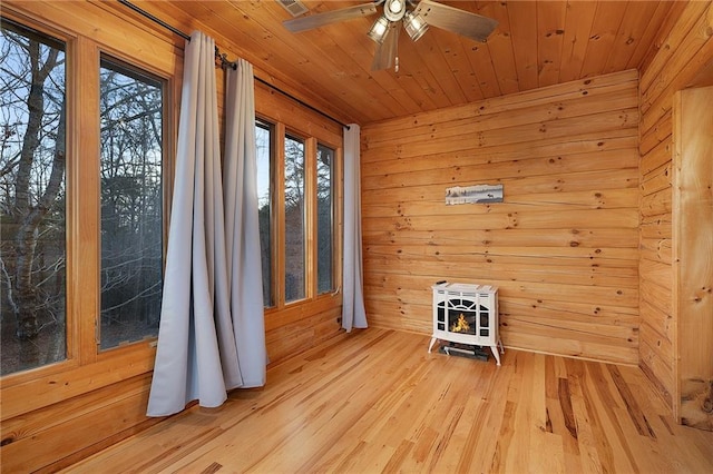 interior space featuring light wood-type flooring, a wood stove, ceiling fan, wooden ceiling, and wooden walls