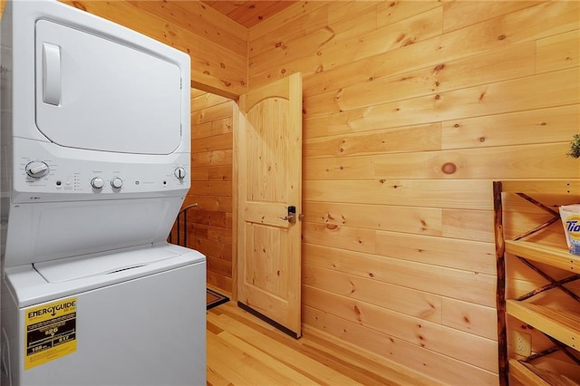 laundry room with light hardwood / wood-style floors, stacked washer / dryer, and wood walls