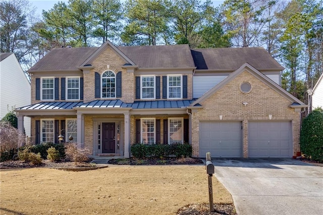 colonial-style house featuring driveway, a standing seam roof, an attached garage, brick siding, and metal roof