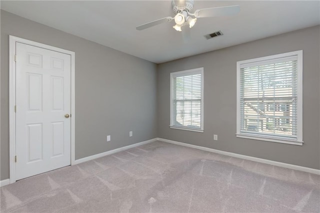 empty room with baseboards, ceiling fan, visible vents, and light colored carpet