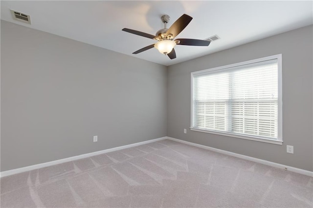 unfurnished room with a ceiling fan, light colored carpet, visible vents, and baseboards