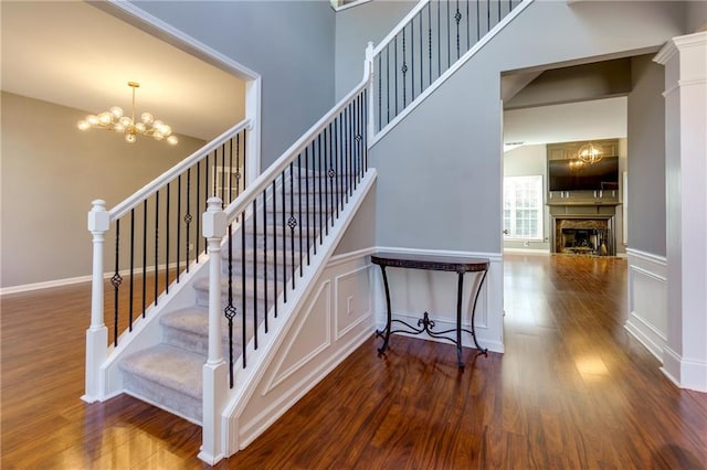 staircase featuring wood finished floors, a fireplace, a chandelier, baseboards, and a towering ceiling