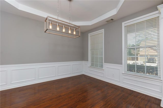 spare room with a wainscoted wall, a tray ceiling, dark wood finished floors, and visible vents