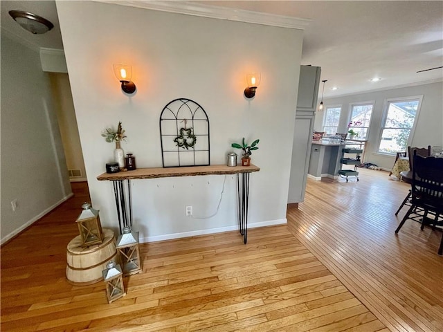 hallway featuring light wood-style flooring, visible vents, baseboards, and crown molding