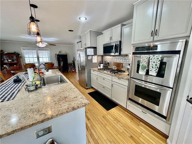 kitchen with decorative backsplash, hanging light fixtures, stainless steel appliances, light wood-style floors, and a sink