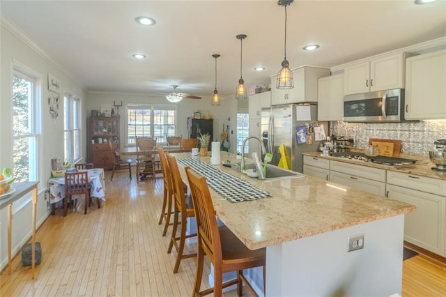 kitchen featuring decorative backsplash, stainless steel appliances, crown molding, light wood-type flooring, and a sink