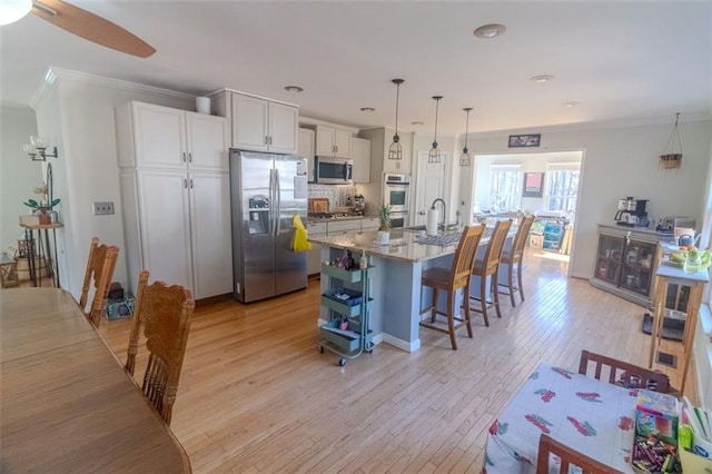 kitchen with light stone counters, decorative light fixtures, appliances with stainless steel finishes, an island with sink, and white cabinets