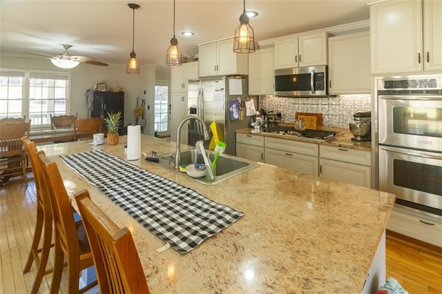 kitchen featuring appliances with stainless steel finishes, pendant lighting, tasteful backsplash, sink, and a kitchen island with sink