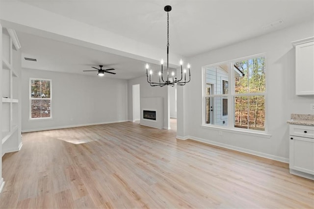 unfurnished living room featuring ceiling fan with notable chandelier, light hardwood / wood-style floors, and plenty of natural light