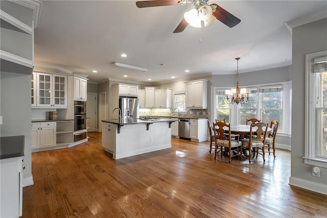 kitchen featuring tasteful backsplash, appliances with stainless steel finishes, white cabinetry, and a center island with sink