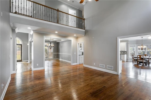 unfurnished living room with dark wood-type flooring, a high ceiling, plenty of natural light, and ceiling fan with notable chandelier