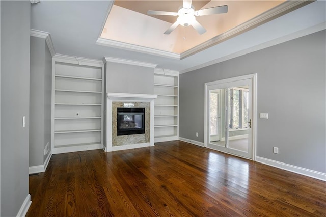 unfurnished living room with dark hardwood / wood-style floors, built in features, ornamental molding, ceiling fan, and a raised ceiling