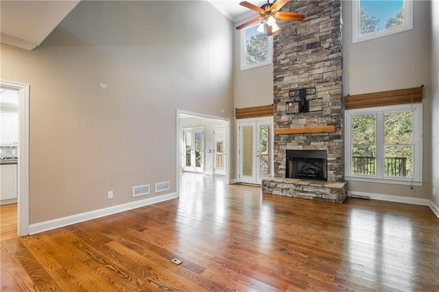 unfurnished living room featuring hardwood / wood-style flooring, a stone fireplace, ceiling fan, a towering ceiling, and ornamental molding