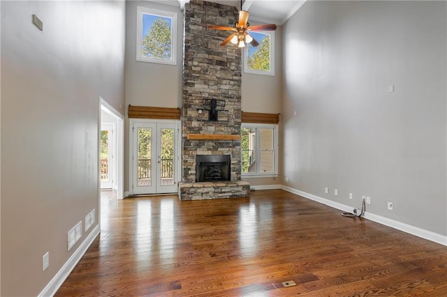 unfurnished living room featuring a stone fireplace, a towering ceiling, wood-type flooring, ceiling fan, and french doors