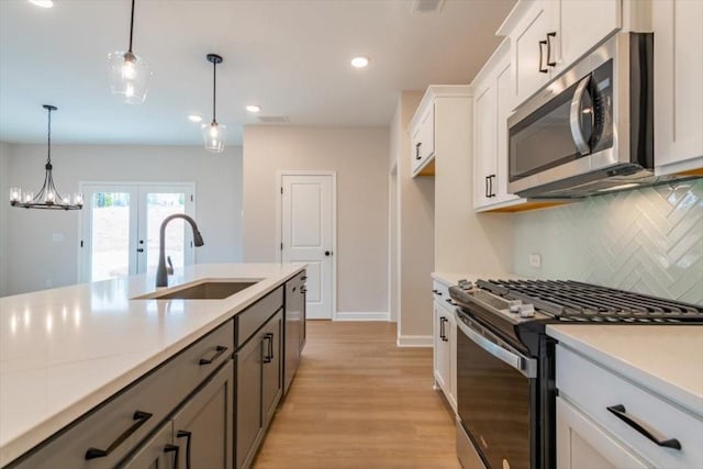 kitchen with sink, white cabinetry, decorative light fixtures, stainless steel appliances, and backsplash