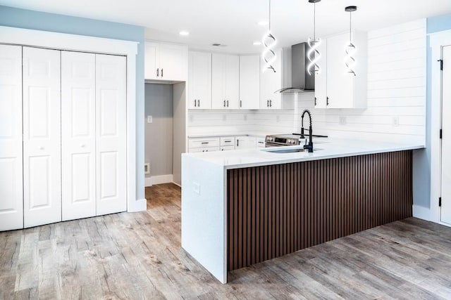 kitchen featuring light wood-style flooring, a peninsula, wall chimney exhaust hood, and a sink