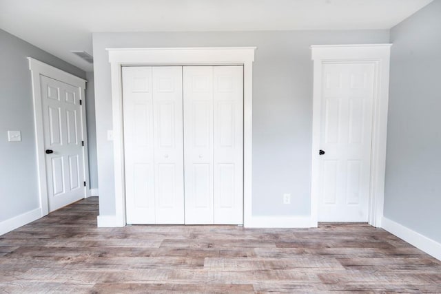 unfurnished bedroom with a closet, visible vents, baseboards, and wood finished floors