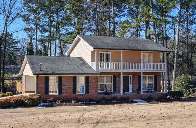 view of front facade with covered porch, brick siding, roof with shingles, and a balcony