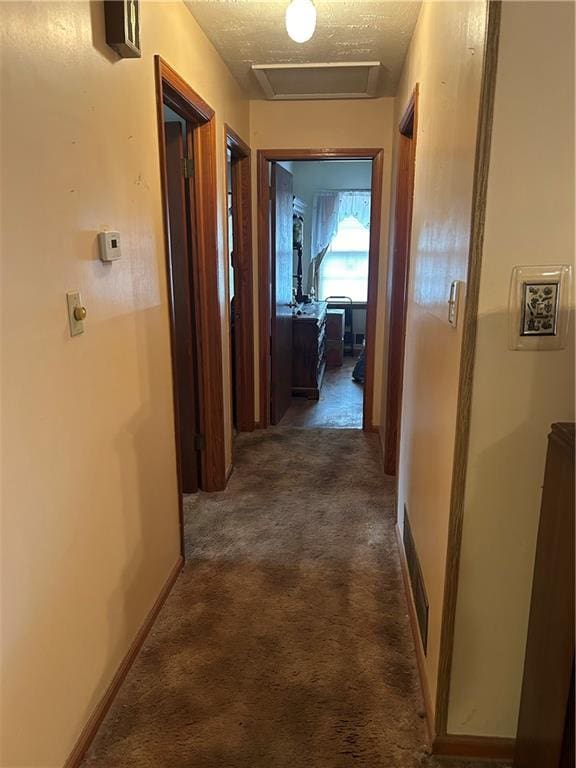 hall with a textured ceiling and dark colored carpet