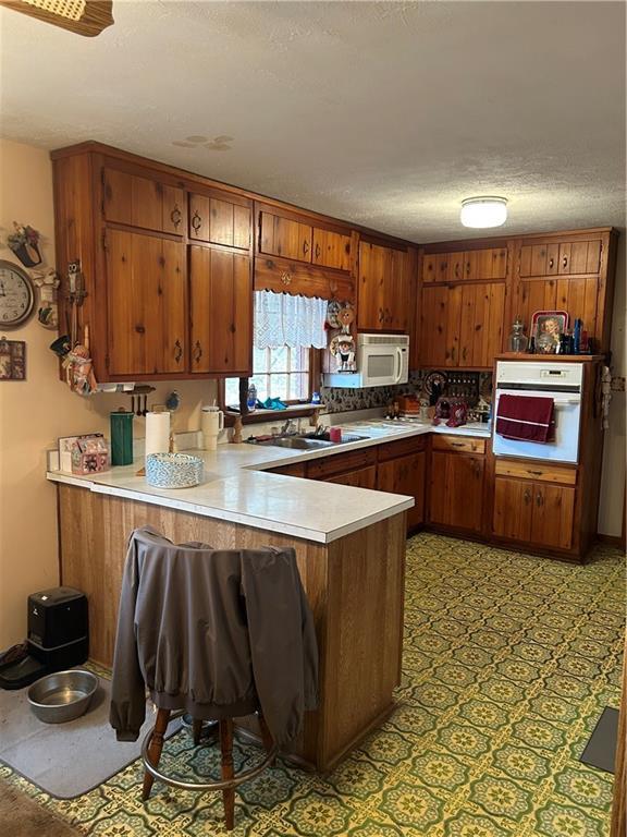 kitchen with kitchen peninsula, sink, white appliances, a kitchen breakfast bar, and a textured ceiling