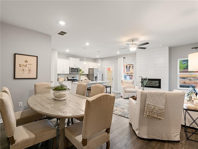 dining area featuring ceiling fan, dark wood-type flooring, and a fireplace