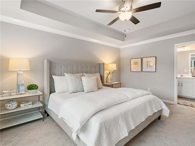 carpeted bedroom with ceiling fan, ensuite bathroom, and a raised ceiling