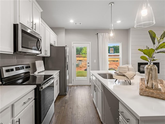 kitchen with hanging light fixtures, stainless steel appliances, white cabinets, a fireplace, and sink