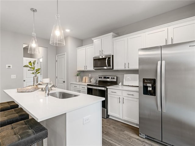 kitchen with pendant lighting, stainless steel appliances, a center island with sink, white cabinets, and sink