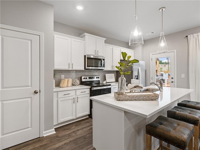 kitchen with hanging light fixtures, a center island with sink, a breakfast bar area, white cabinets, and appliances with stainless steel finishes