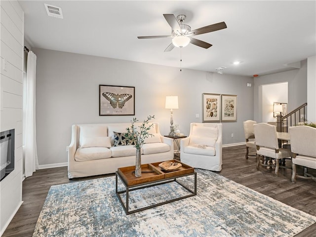 living room featuring ceiling fan, dark wood-type flooring, and a large fireplace