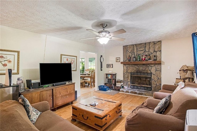 living room with a fireplace, a textured ceiling, light hardwood / wood-style flooring, and ceiling fan